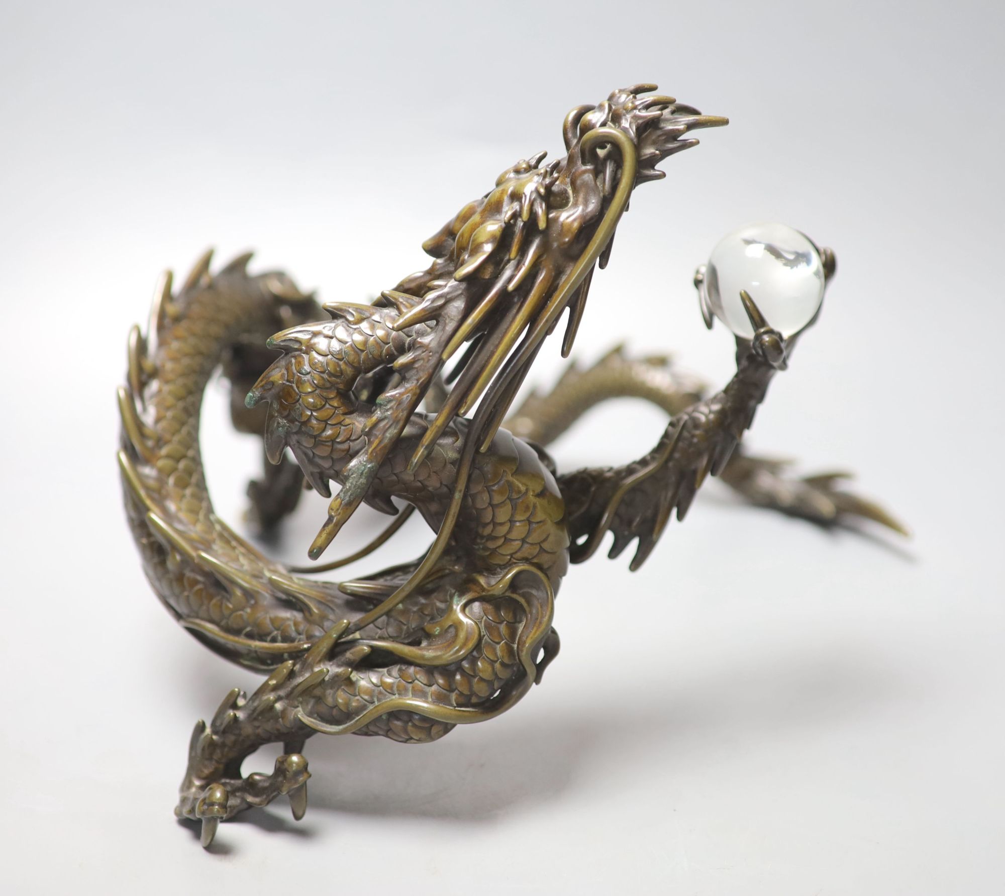 A large Japanese bronze model of a dragon clasping a glass jewel, 29.5cm across